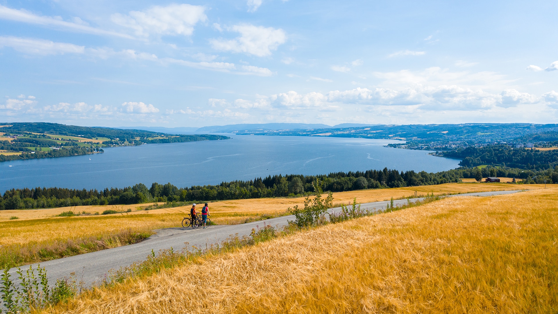 Two people on bikes having a pitstop enjoying the view of Mjøsa on a sunny summer day.