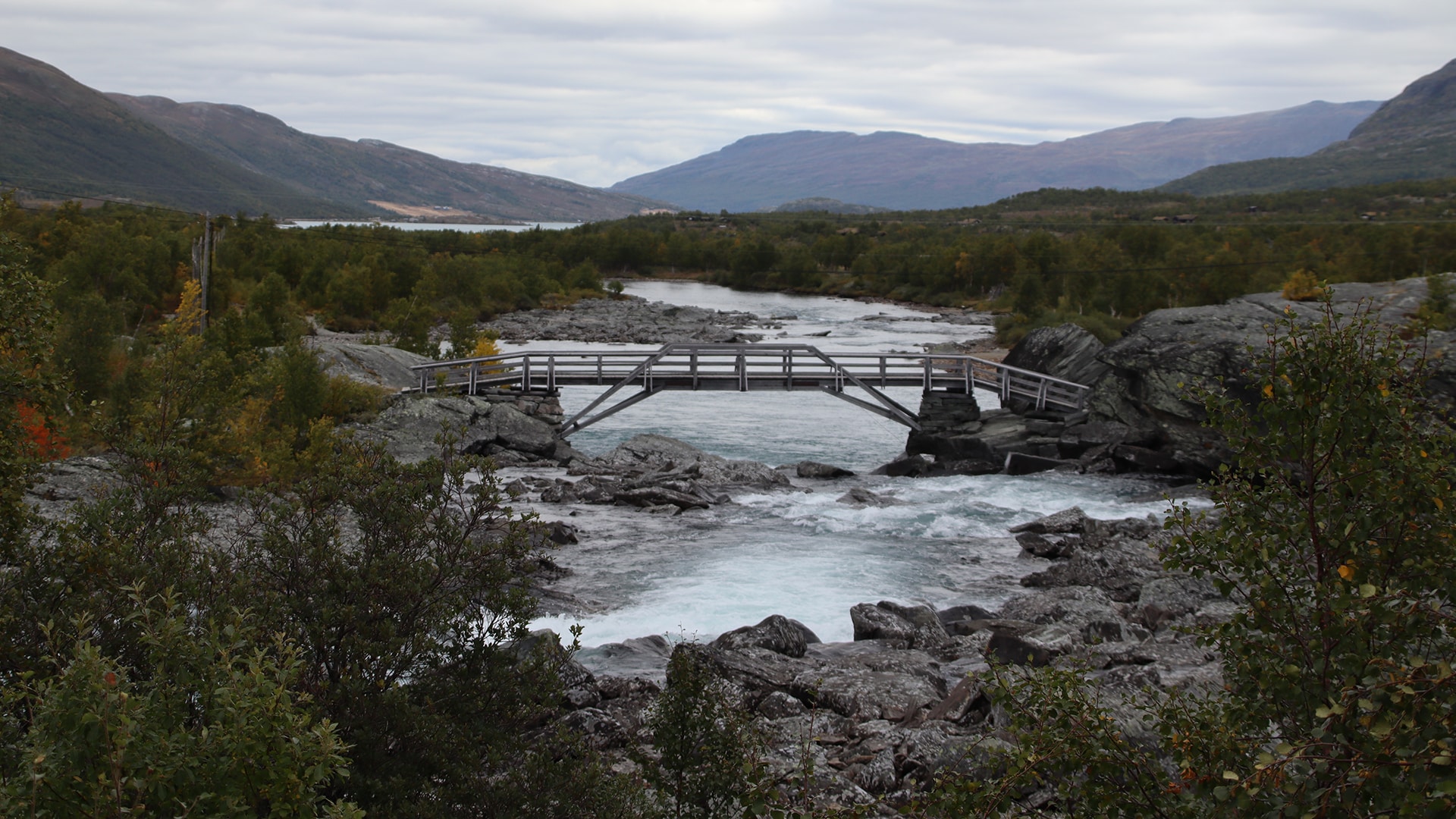 A wooden bridge over a river in Valdres with mountains in the distance.