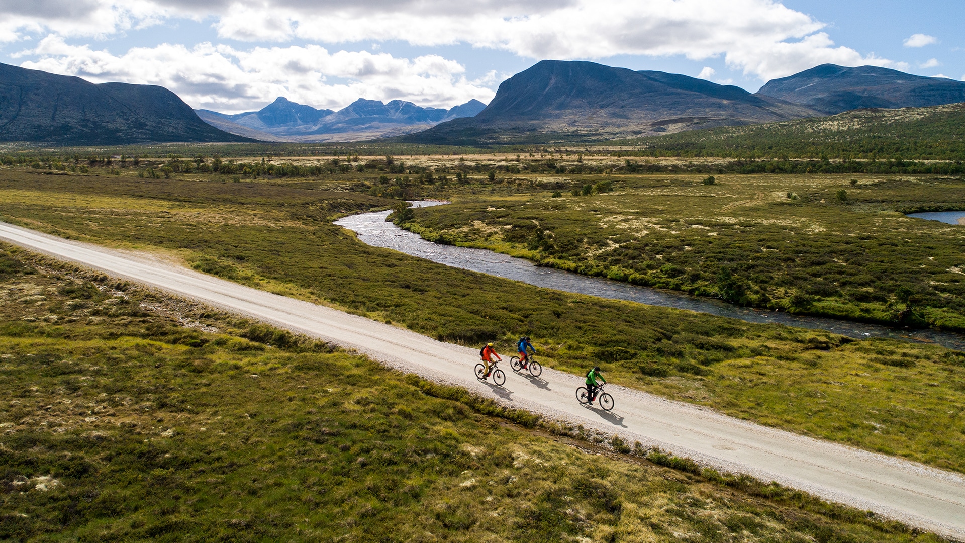 Three people riding bikes on a path in the mountain landscape of Grimsdalen.