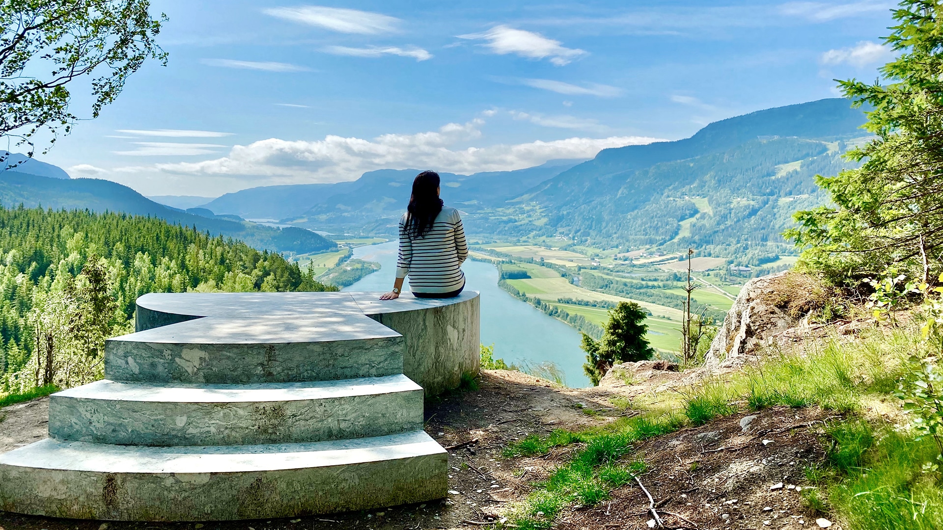 A woman enjoying the view of Gudbrandsdalen on a sunny summer day with mountains in the distance.