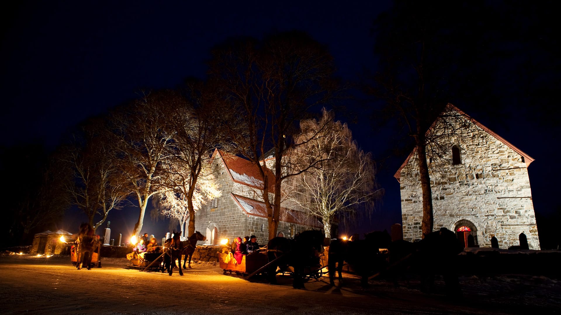 Horses and carriages lit with torches at night in front of the stone buildings of Granavolden Gjæstgiveri.