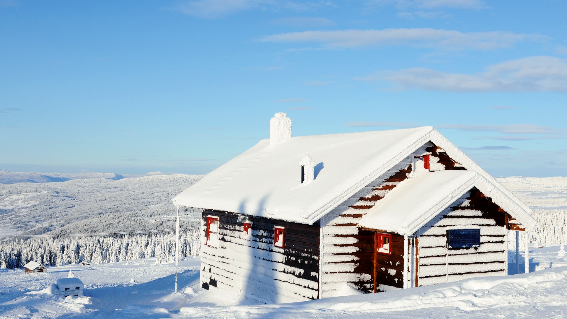 A remote cabin is almost completely covered in snow on a sunny winter day.