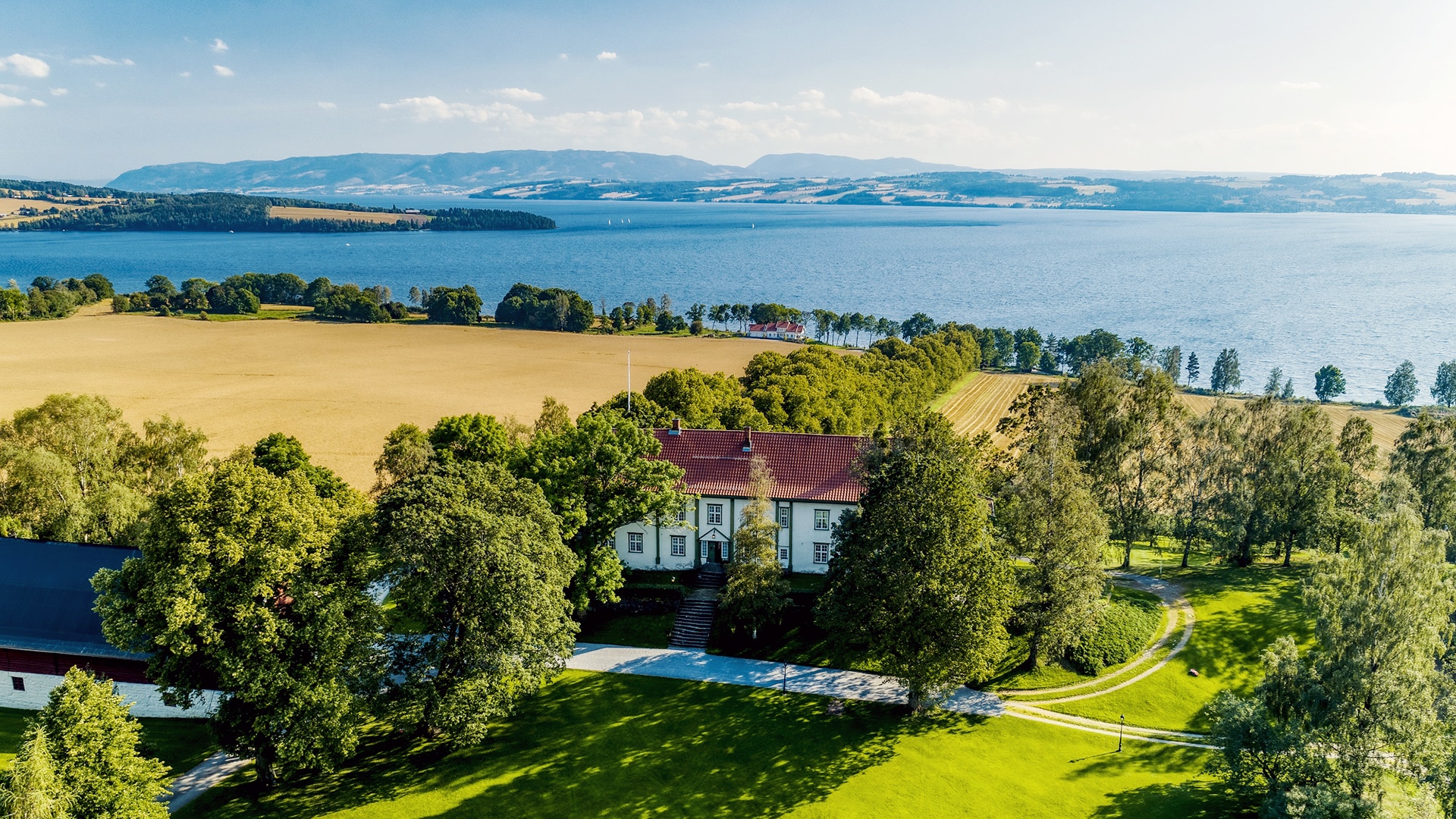 The main house of Hoel farm surrounded by trees and fields in front of Mjøsa.