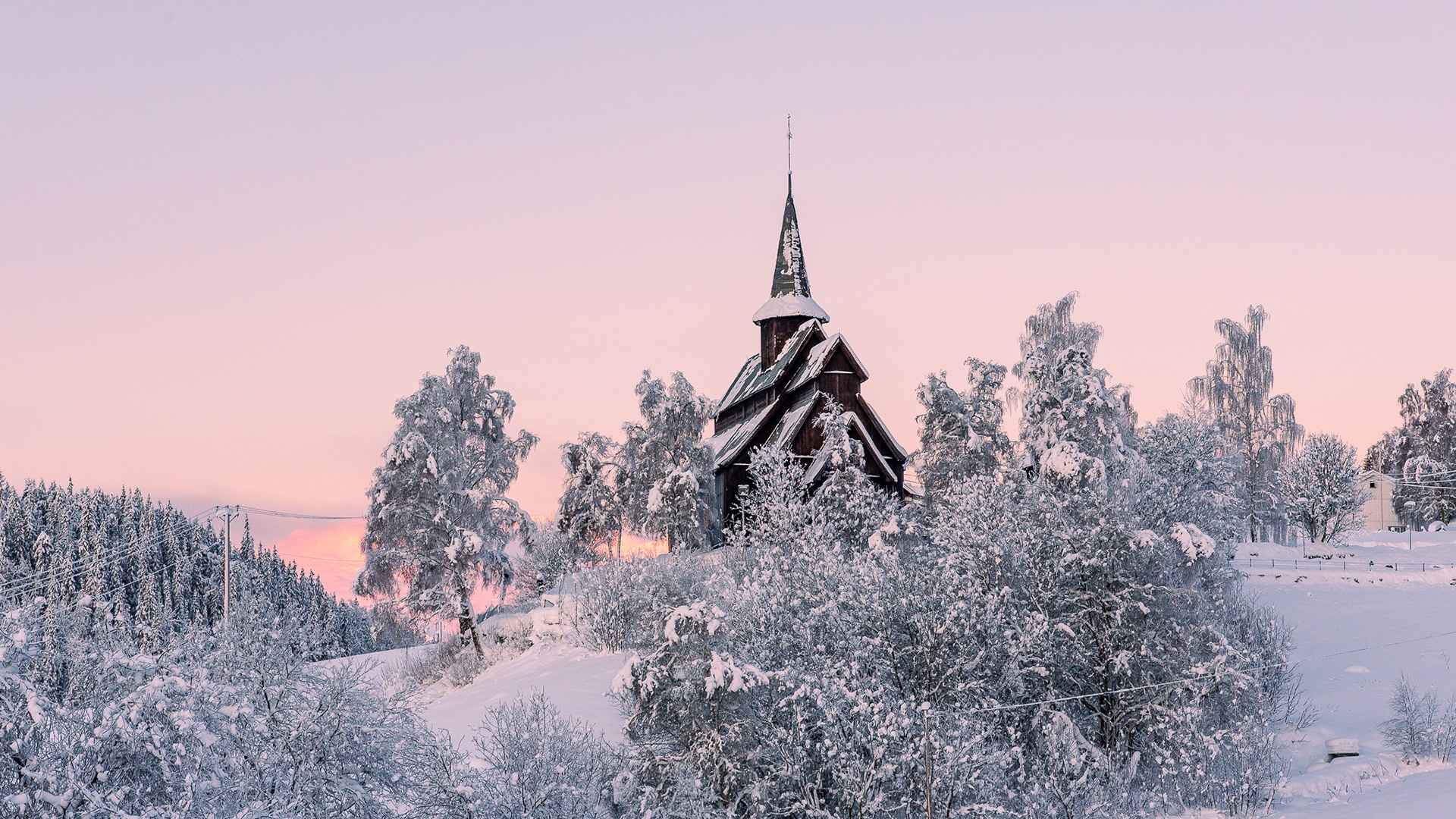 The stave church of Høre covered in snow at sunset on a winter day.
