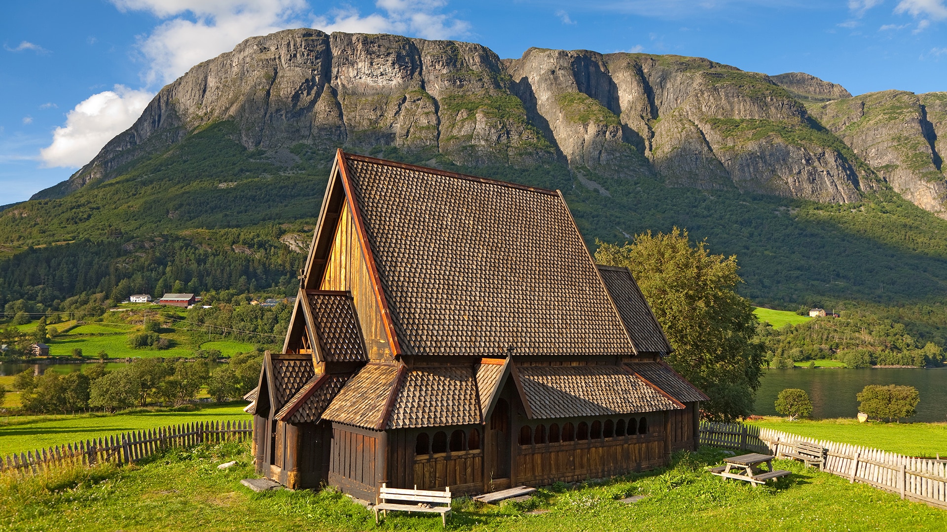 The stave church of Øye on a sunny summer day with a tall mountain behind.