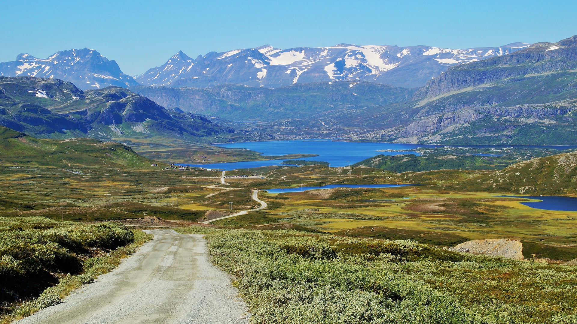 The winding dirt road Slettefjellvegen with snow covered high mountains in the back.