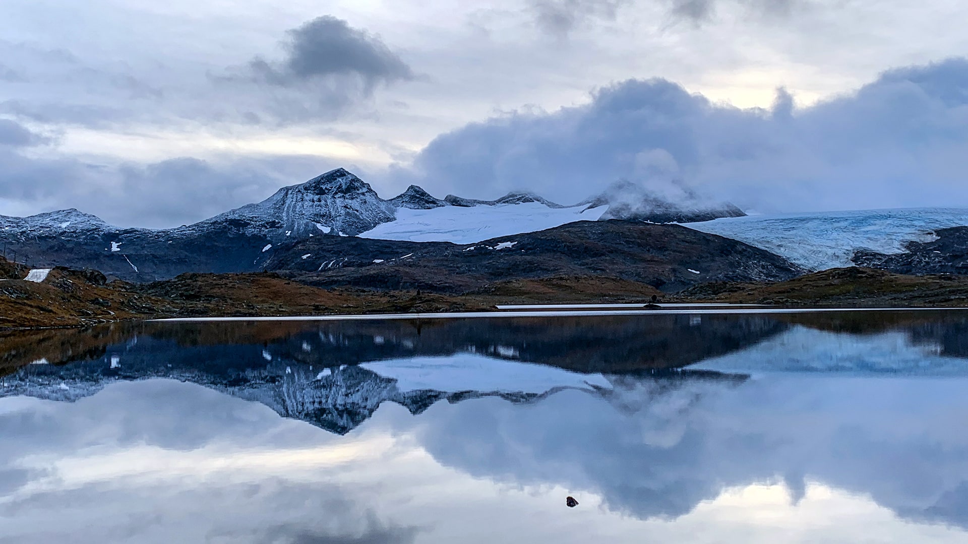 The mountains of Sognefjellet covered in snow and clouds is reflecting in a lake.