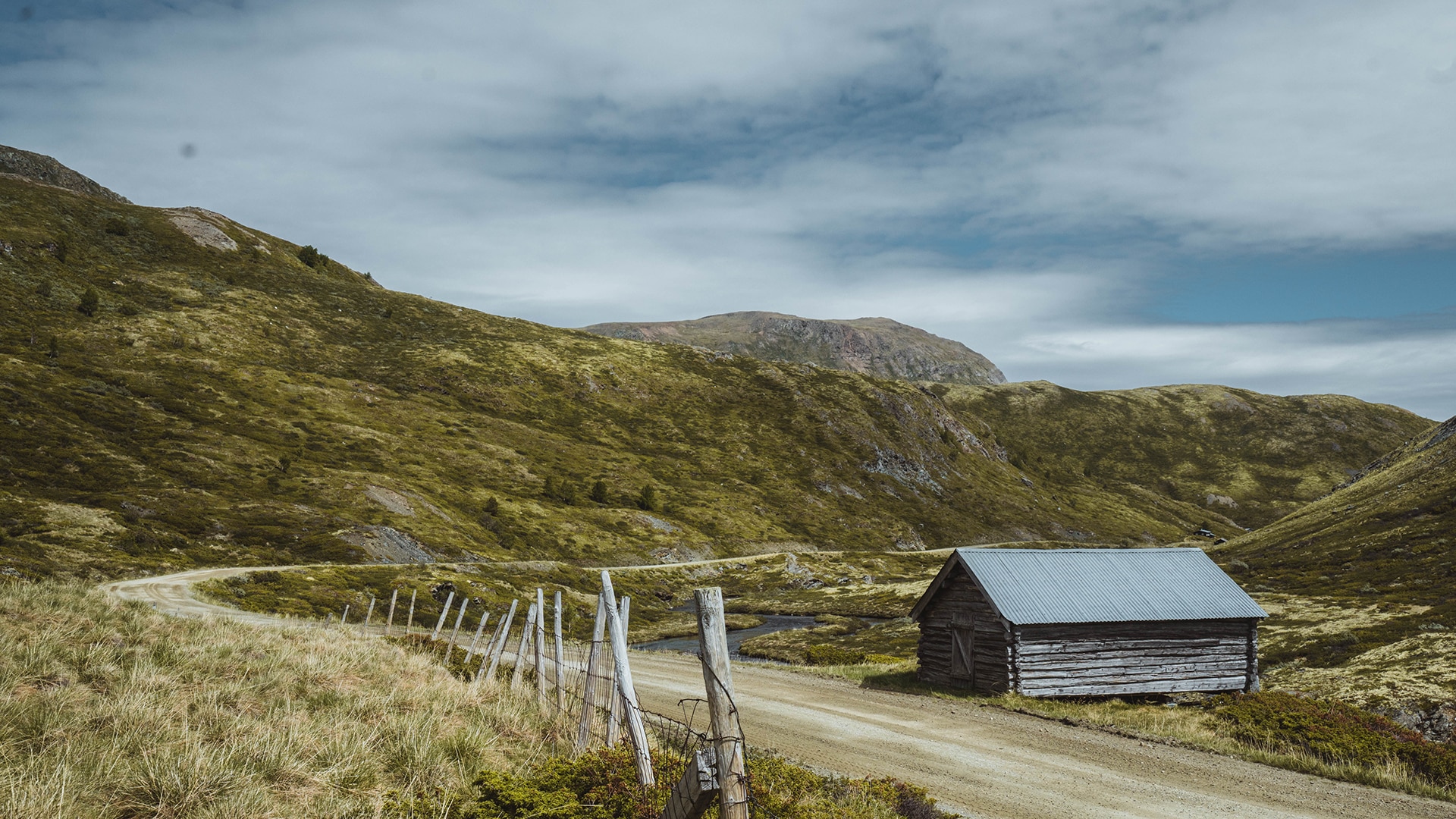 An old remote laft house next to a winding dirt road surrounded by mountains on Dovre.