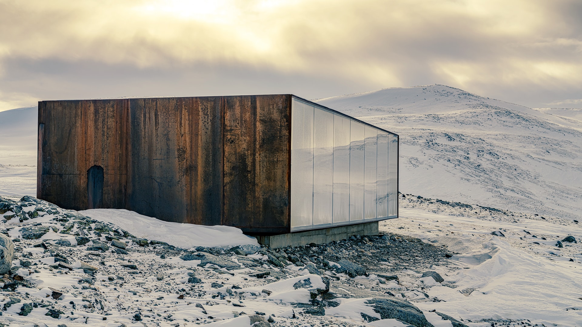 A building with big windows in front of the snow covered mountain Snøhetta on Dovrefjell.
