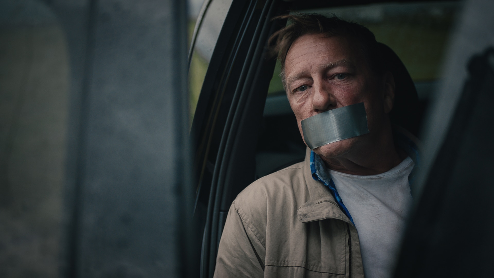 A man with duck tape on his mouth sitting in the back of a car from the movie Jakten På Olavsskrinet.